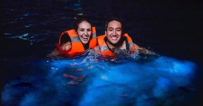 Happy couple swimming in bioluminescent waters with life vests