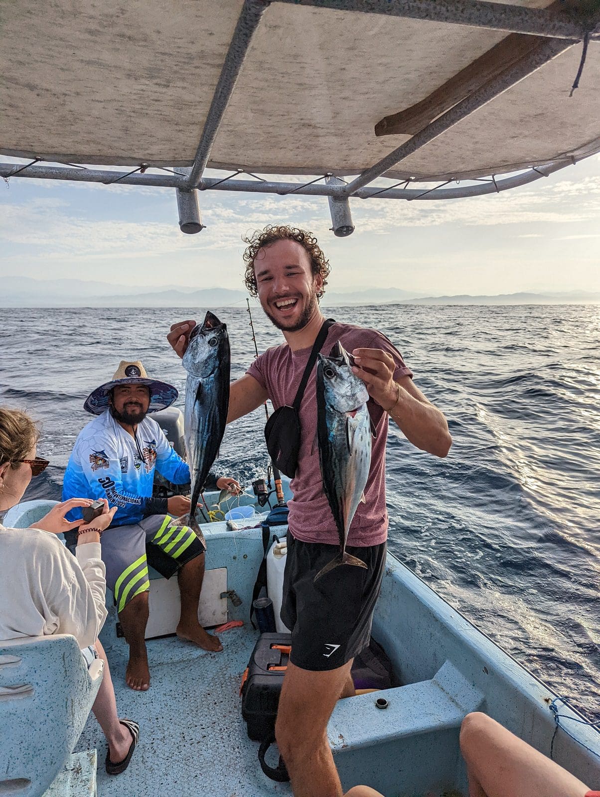 Smiling angler holding two skipjack tuna on fishing boat