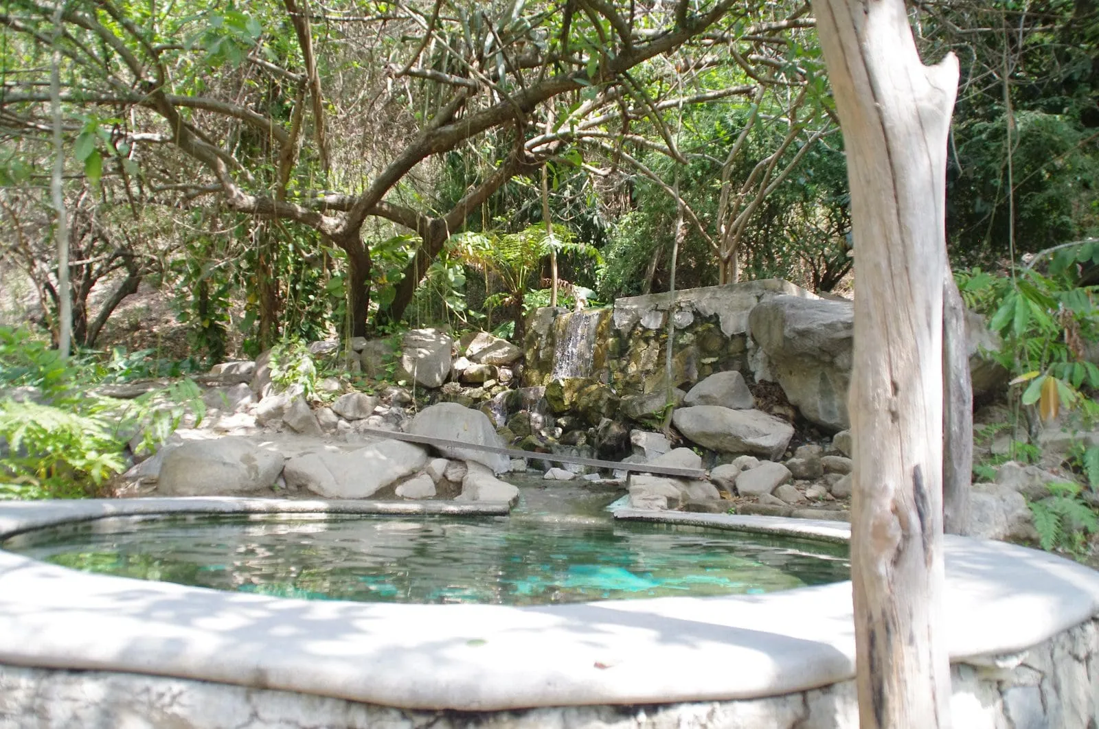 Natural hot springs pool with small waterfall and lush vegetation