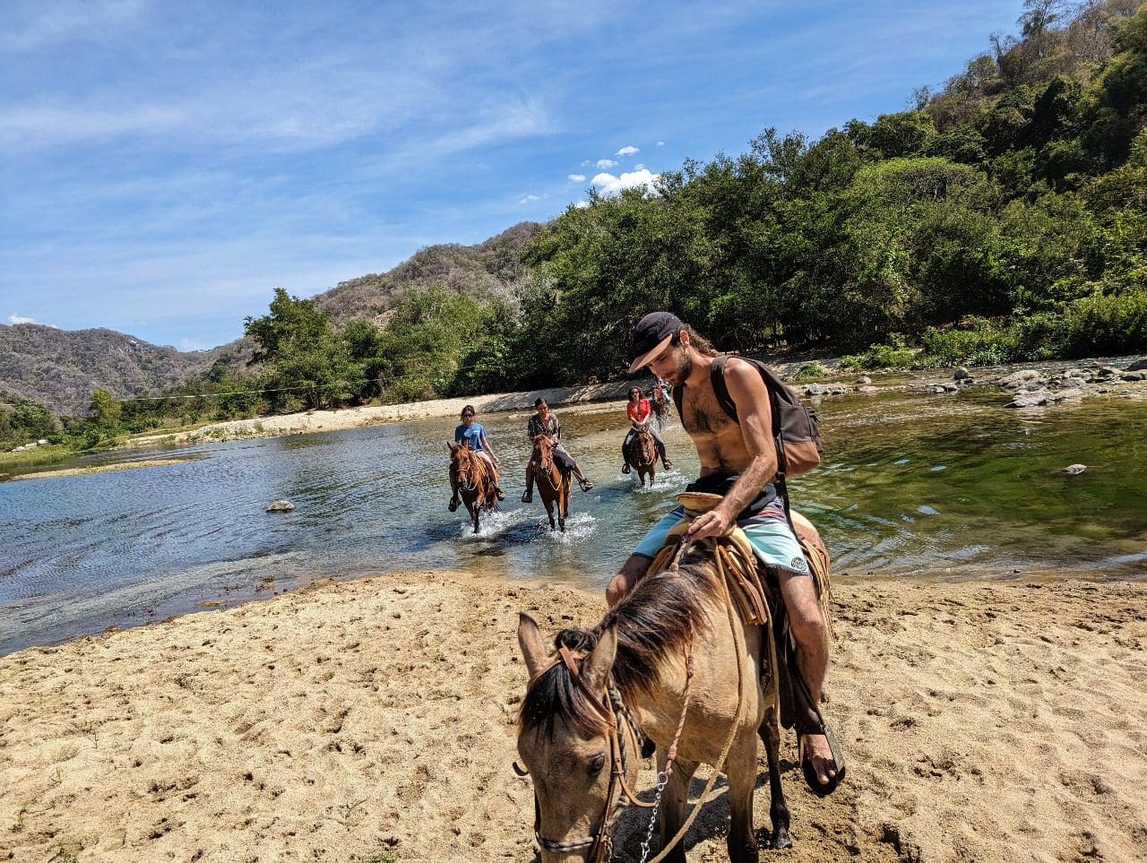 Group crossing river on horseback with mountain backdrop