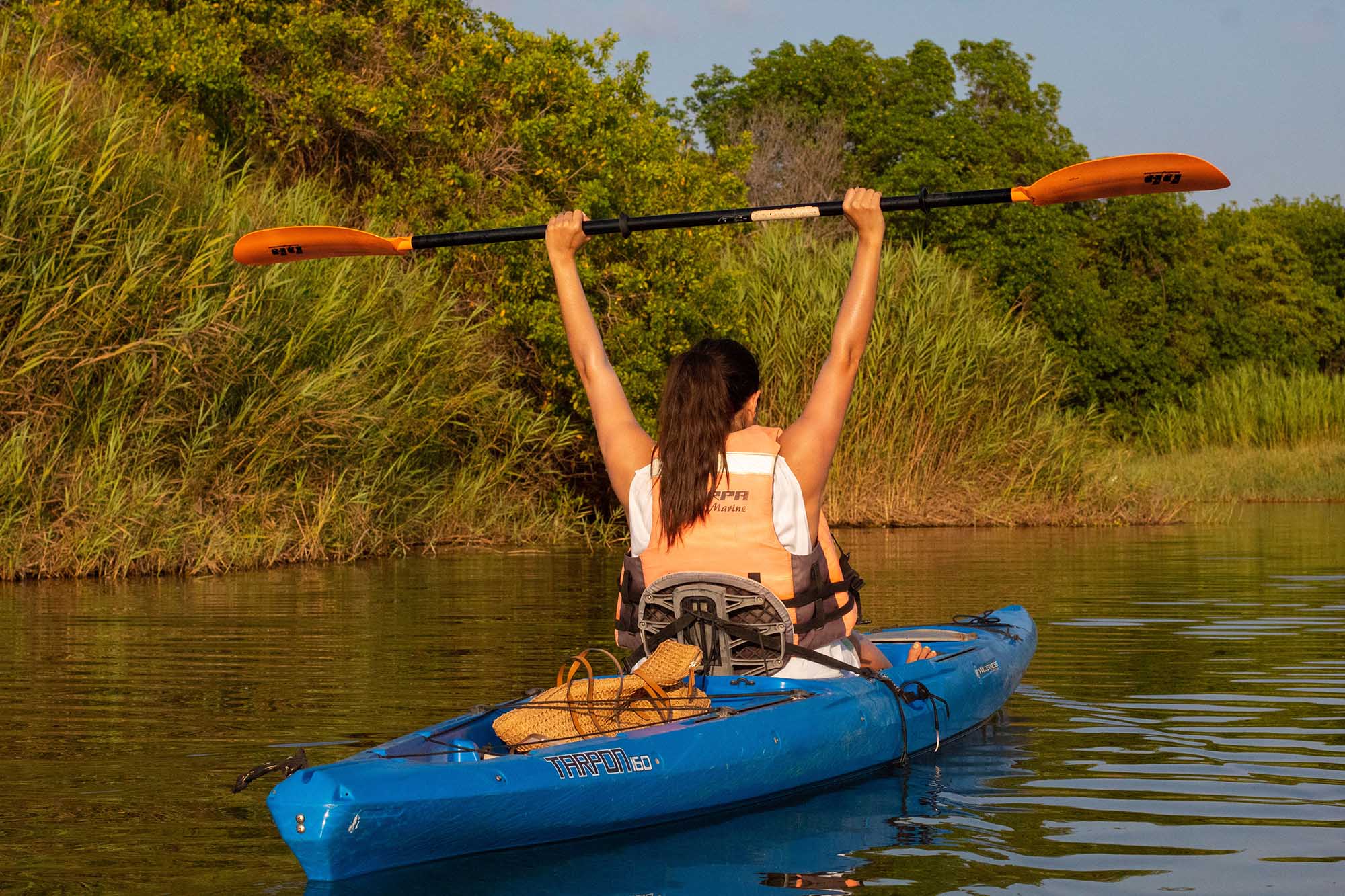 Woman raising paddle in celebration on blue kayak