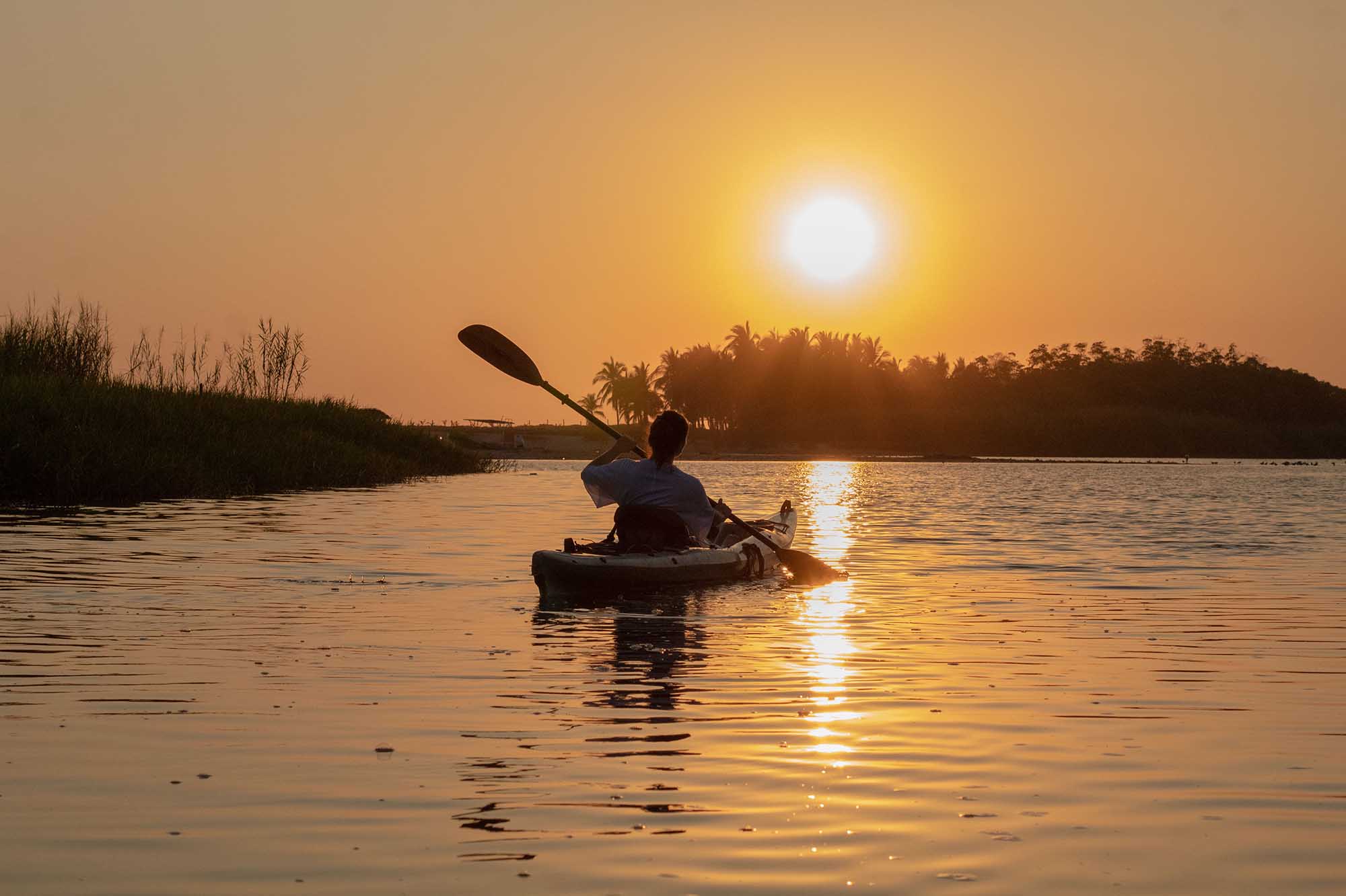 Silhouette of kayaker paddling at golden sunset